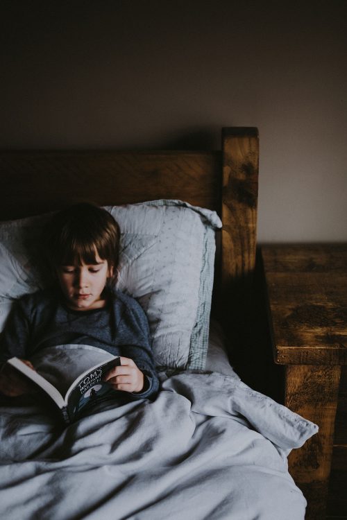 Foto de un niño en la cama leyendo un libro.