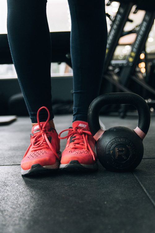 Foto de los pies de una mujer en zapatillas junto a una pesa en un gimnasio.