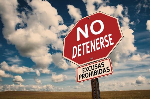 Foto de un cartel vial que en lugar de decir "STOP" dice "No detenerse" y debajo "Excusas prohibidas." De fondo una llanura y un cielo soleado con algunas nubes