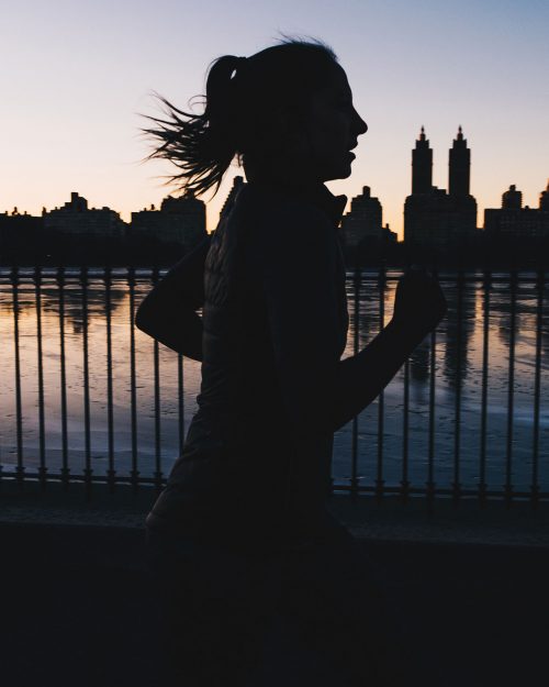 La silueta de una chica corriendo en un parque urbano justo antes de que amanezca o en las últimas horas del día