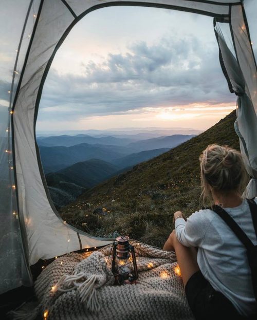 Una niña mirando un paisaje de montaña desde adentro de una carpa con luces