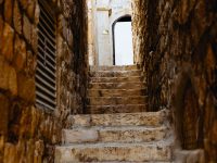 Una escalinata en un pasillo angosto que conduce a una puerta abierta donde se observa el cielo