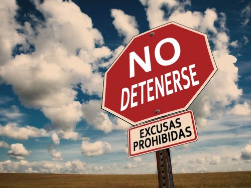 Foto de un cartel vial que en lugar de decir "STOP" dice "No detenerse" y debajo "Excusas prohibidas." De fondo una llanura y un cielo soleado con algunas nubes