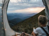 Una niña mirando un paisaje de montaña desde adentro de una carpa con luces