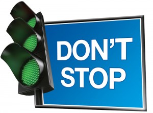 Semáforo con las tres luces en verde, junto a un cartel que dice "Don't Stop" ("No te detengas" en inglés)